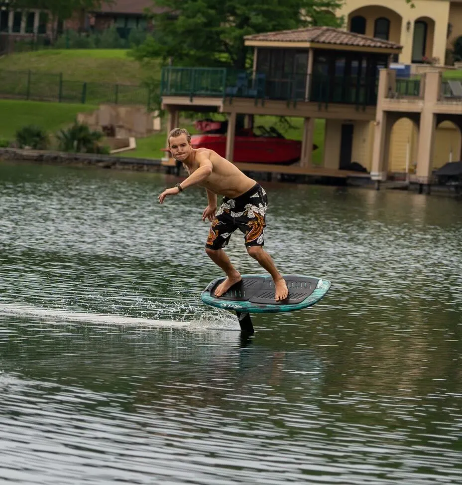 Man riding a hydrofoil board on Lake Austin near waterfront homes.